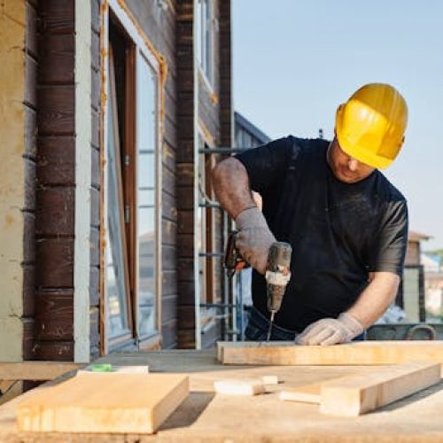 A construction worker using a power drill on a building site, outdoors during the day.